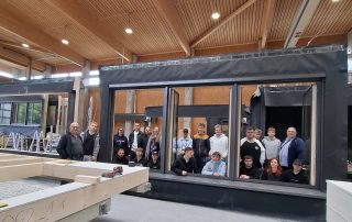 Azubis schauen durch Holz-Alu-Fenster in Montagehalle