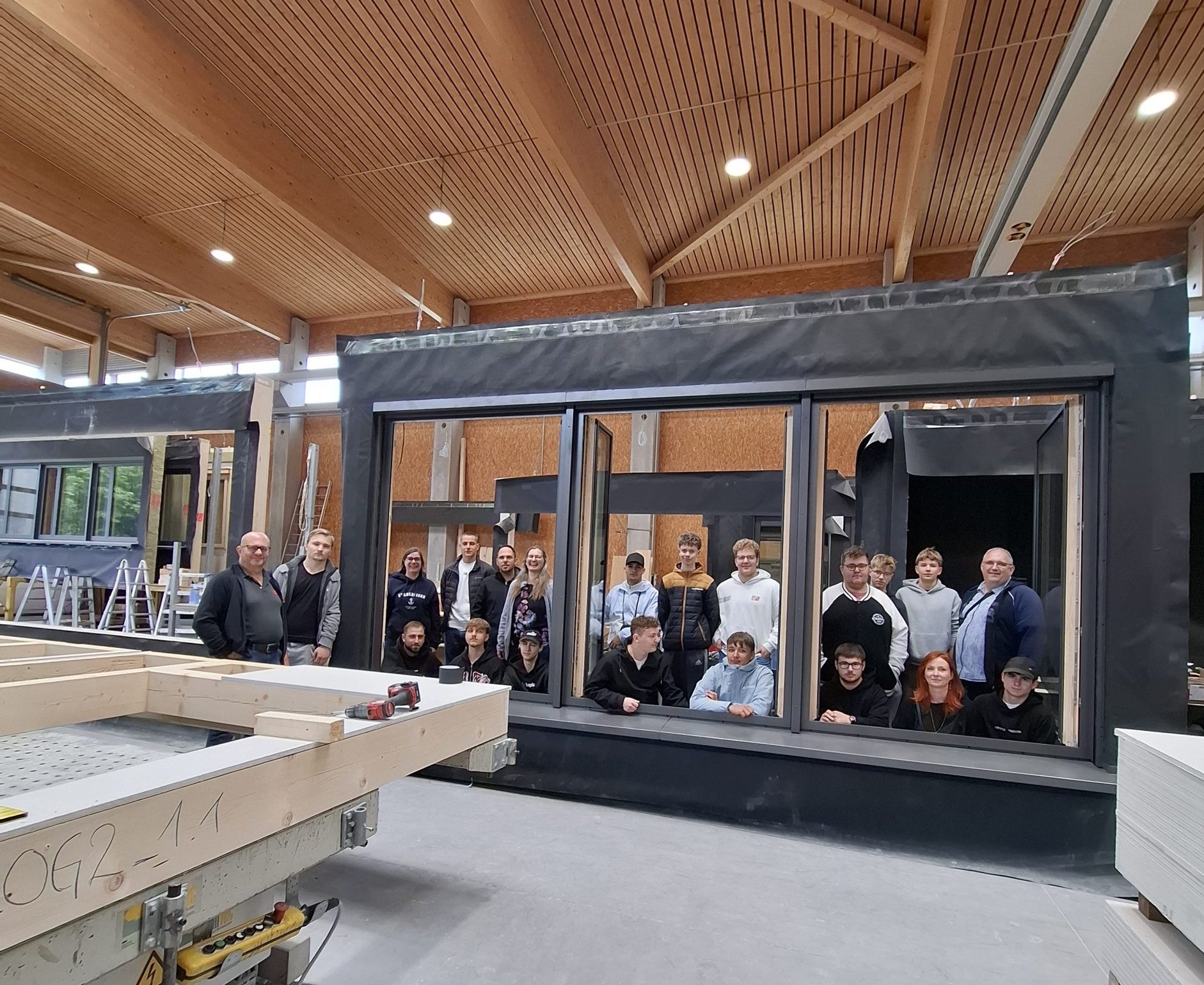 Azubis schauen durch Holz-Alu-Fenster in Montagehalle